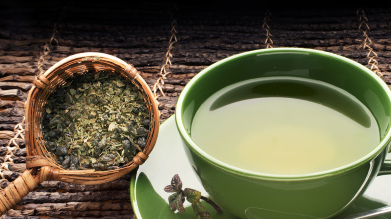 Cup of green tea next to tea leaves