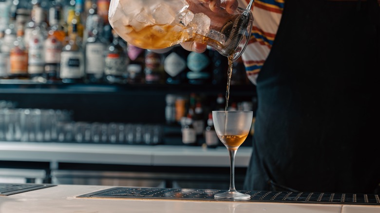 Bartending pouring cocktail into a Nick & Nora glass.