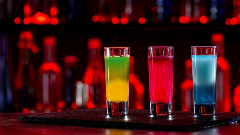 Bright colored cocktail shots at a bar with red backlights.