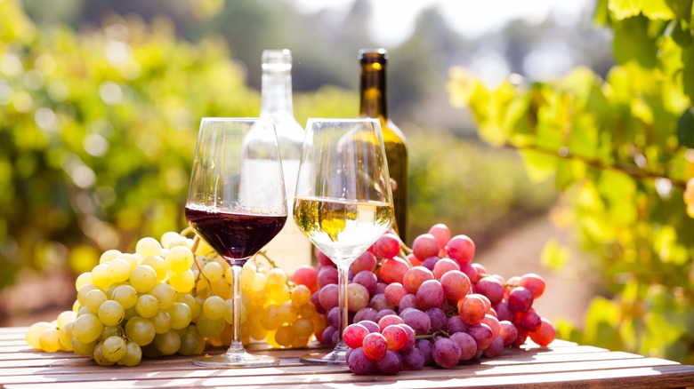 Glass of red and glass of white on a table next to grapes.