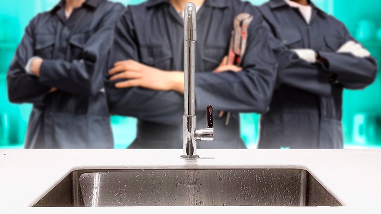 Three plumbers with their arms crossed standing behind a kitchen sink