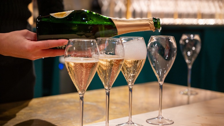 Hand pouring Champagne into glasses at bar
