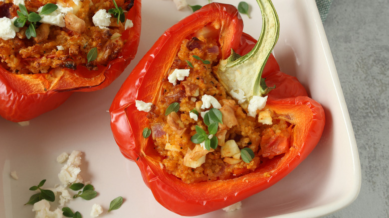 Stuffed red bell pepper with crumbled feta and herb garnish on a white plate