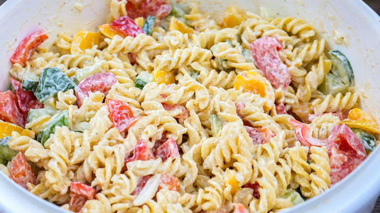 Creamy pasta salad in large white bowl with chunks of tomatoes and bell peppers