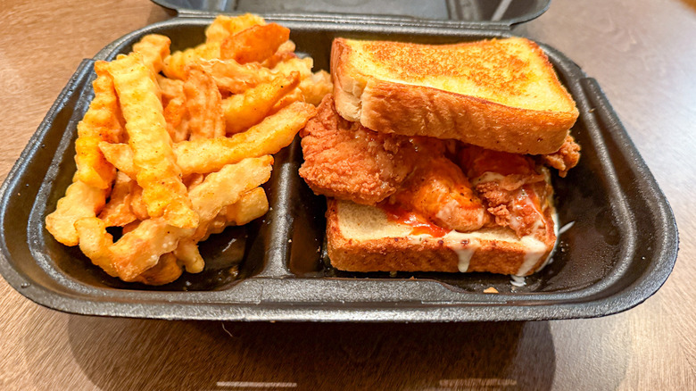 Zaxby's Kickin' Chicken Sandwich and side of French fries in a black takeout container