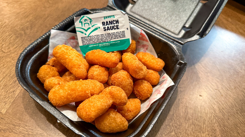 Fried white cheddar bites in a black takeout container