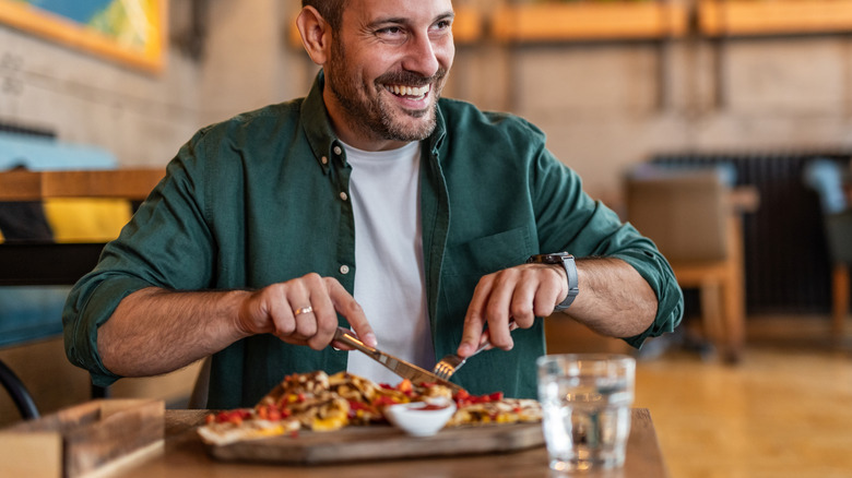 Smiling man cutting into plate of food at a restaurant