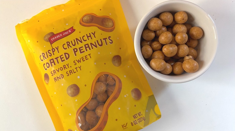 Trader Joe's Crispy Crunchy Coated Peanuts sit in a small white bowl next to a package on a white table.