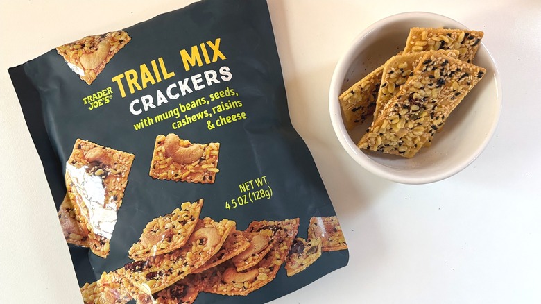 Trader Joe's Trail Mix Crackers sit in a small white bowl next to a package on a white table.