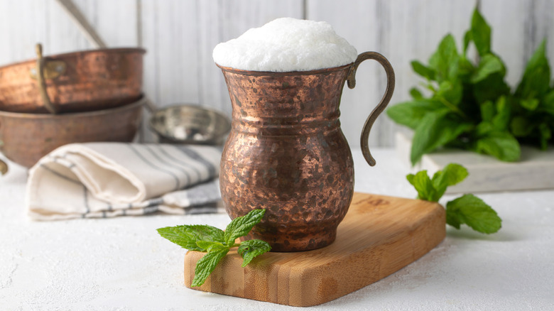 copper cup of ayran on a wooden board next to mint leaves