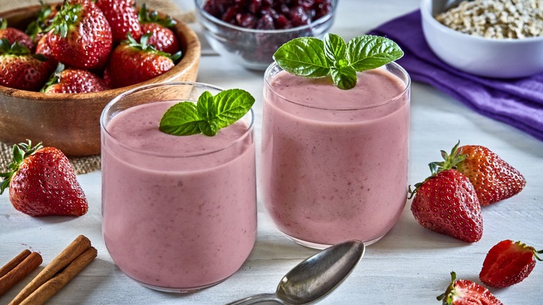 Two berry smoothies with strawberries and other ingredients surrounding it
