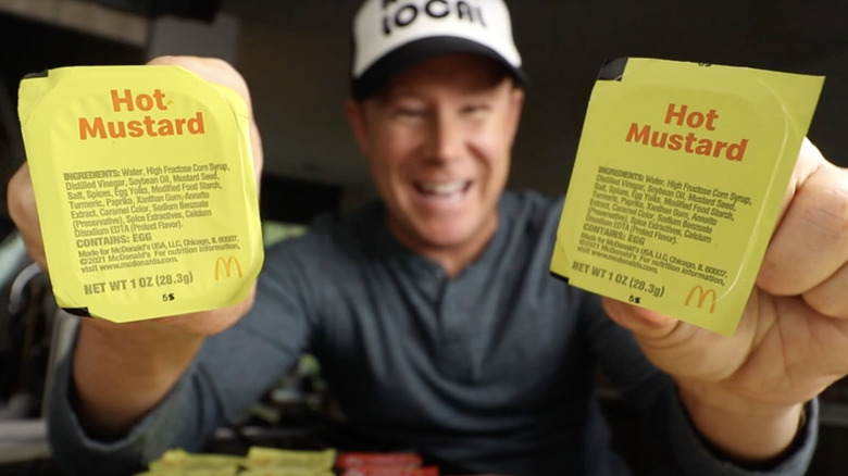 A smiling man holding two packages of McDonald's Hot Mustard Sauce