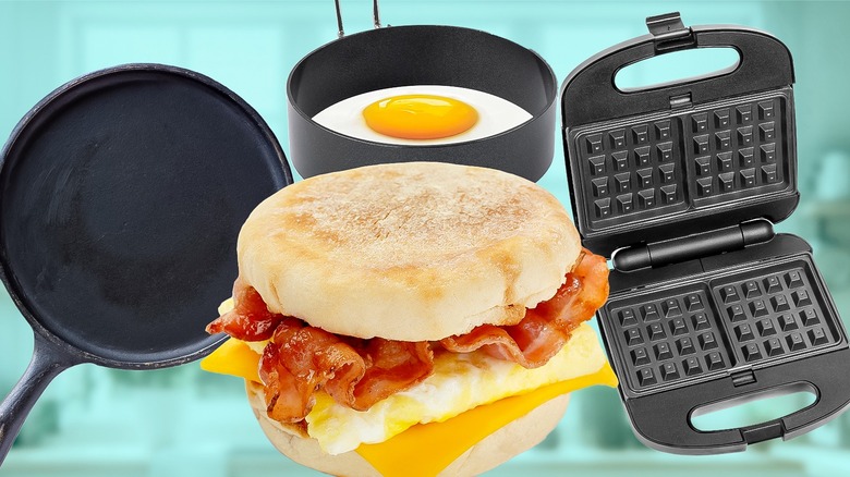 A breakfast sandwich with bacon egg and cheese in front of a pan, an egg cooking in an egg ring, and a waffle iron