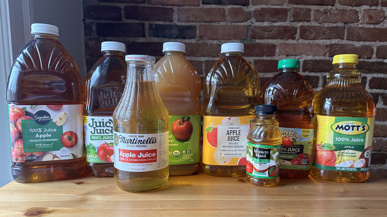 Variety of apple juice bottles on wooden table with brick background
