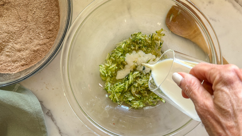 Hand adding milk to bowl of grated zucchini