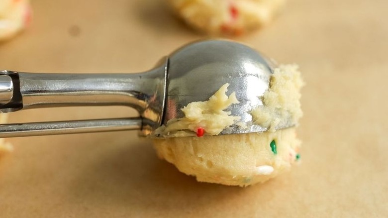 Scoop placing cookie dough ball onto baking sheet