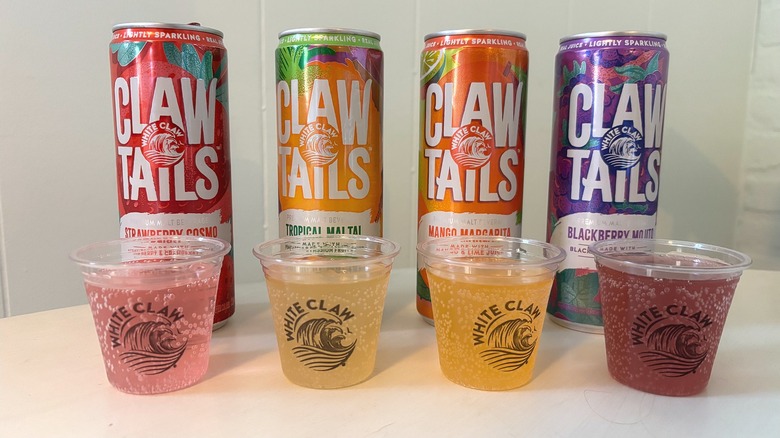Four White Claw ClawTails cans behind tasting cups on a white table