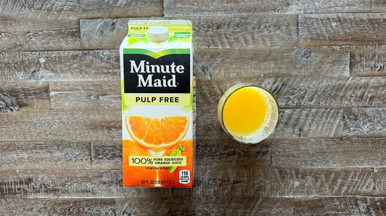 A carton of Minute Maid Pulp Free Orange Juice next to a poured glass