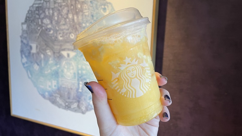 Hand holding the Starbucks Paradise Drink Refresher in front of a painting