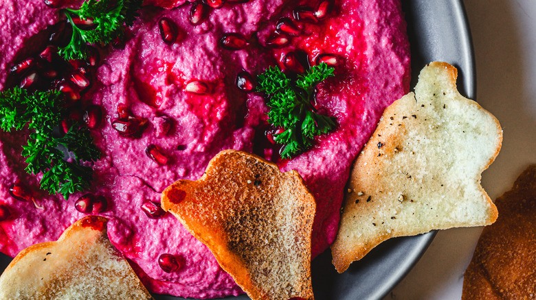 close up on Magenta hummus on a plate with parsley, pomegranate and ghost chips