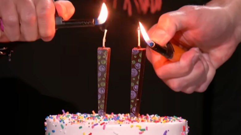 Hands lighting two chocolate candles on a cake
