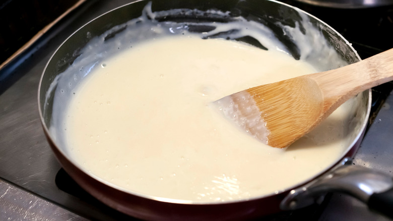 A wooden spoon sits in a pan of white sauce