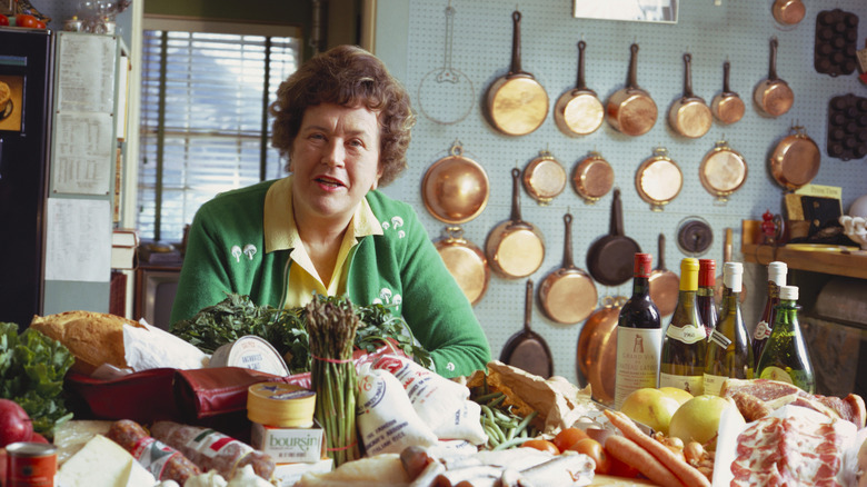 Julia Child posing in her kitchen with lots of food