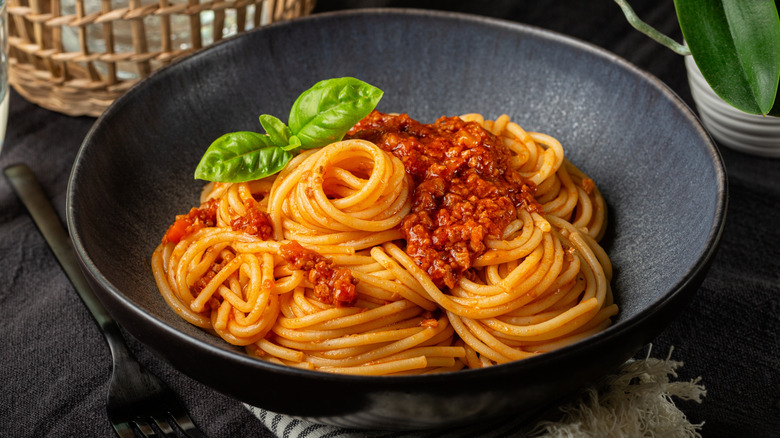 serving of spaghetti bolognese in dark bowl with basil sprig