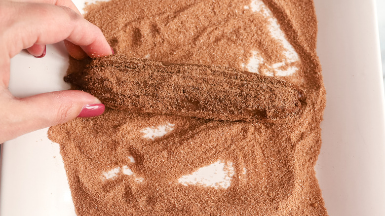chocolate churro being rolled in cinnamon sugar