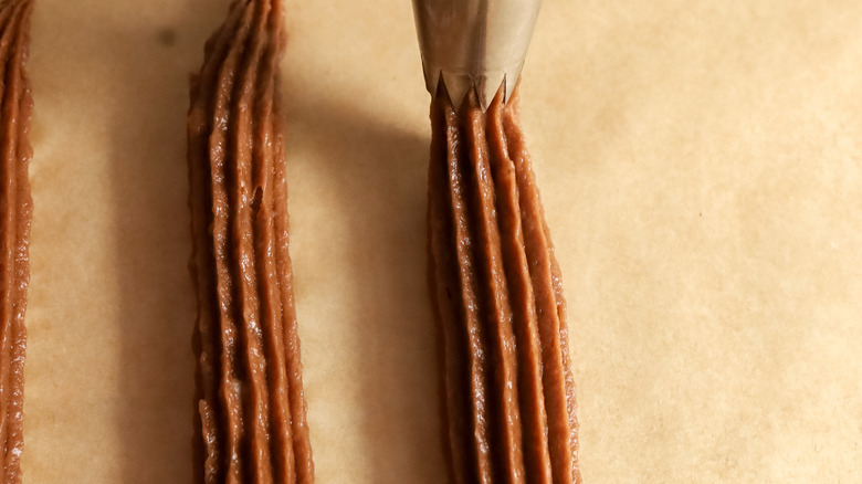 chocolate churros being piped onto a baking sheet