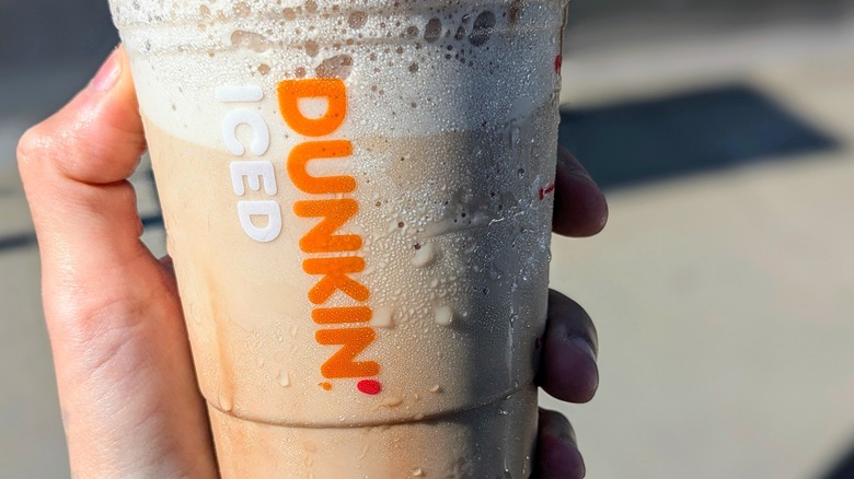 Close-up of a hand holding a sweating plastic cup of Dunkin' frozen coffee