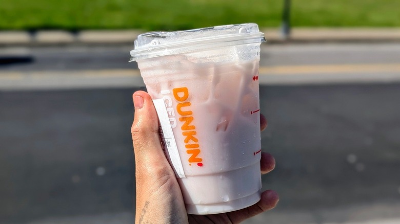Hand holding an iced pink Dunkin' drink outside