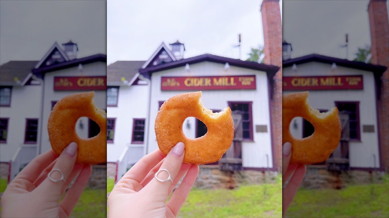 Hand holding donut in front of Clyde's Cider Mill building