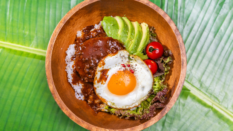 Wooden bowl holding Hawaiian Loco Moco breakfast on top of large leaf