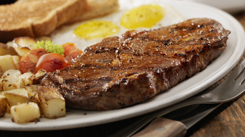 Steak and eggs, potato, toast on white plate