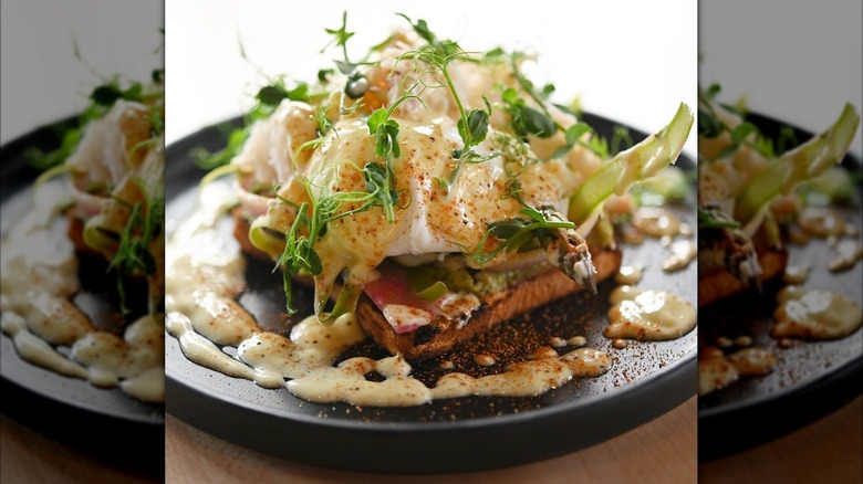 Dungeness crab Benedict topped with microgreens on black plate