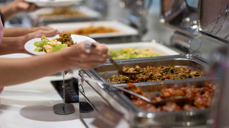 People selecting and scooping food from buffet trays