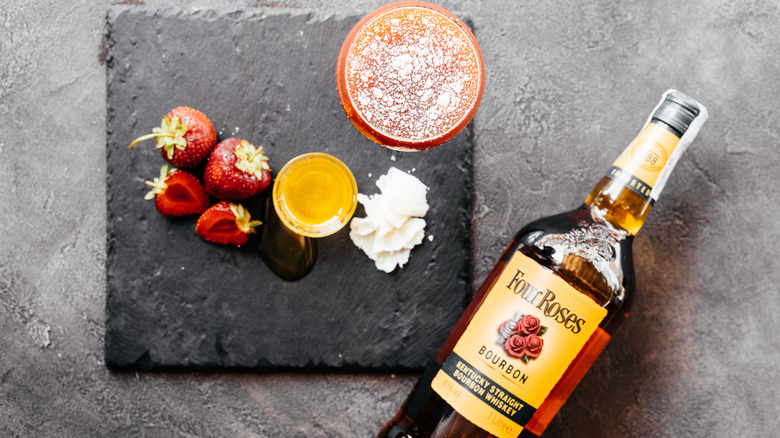 A tray of berries, honey, and a cocktail next to a bottle of Four Roses bourbon