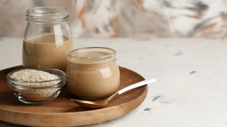 Tahini sauce in jar and bowl of sesame seeds