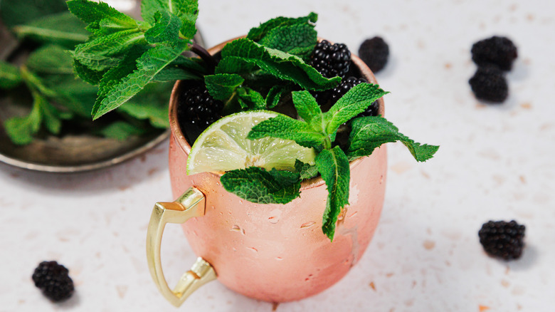 A frosted copper glass of a Kentucky mule with a garnish of mint leaves, blackberries and lime wedges