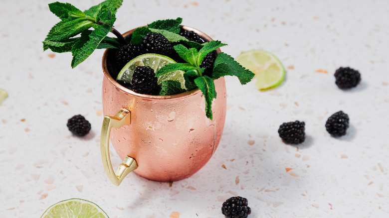 A frosted copper glass of a Kentucky mule with a garnish of mint leaves, blackberries and lime wedges